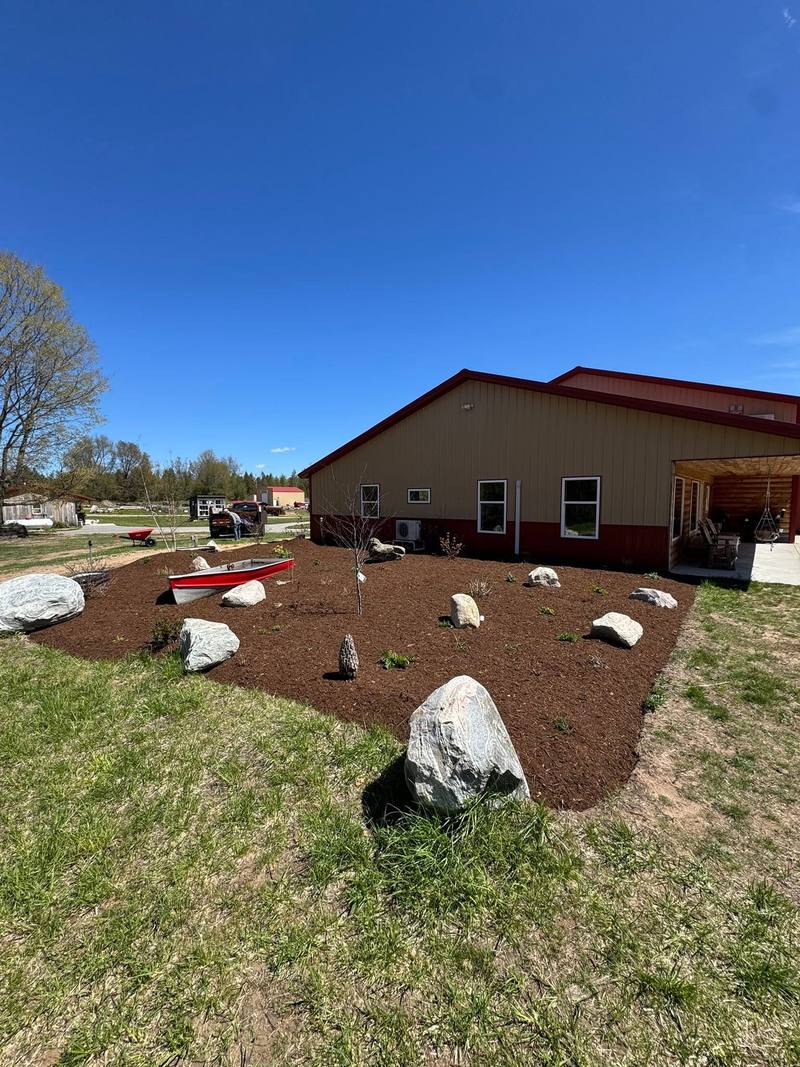 Mulch bed with boulders and new plants next to a red pole barn