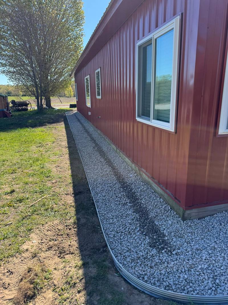 Crushed stone drip edge with metal edging along a red pole barn