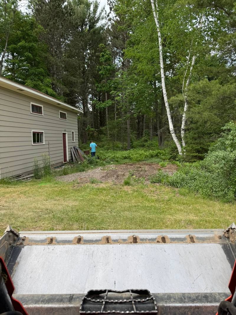 Before: grassy area beside a garage, seen from the skid steer bucket