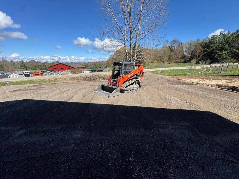 Skid steer grading a wide area next to fresh asphalt