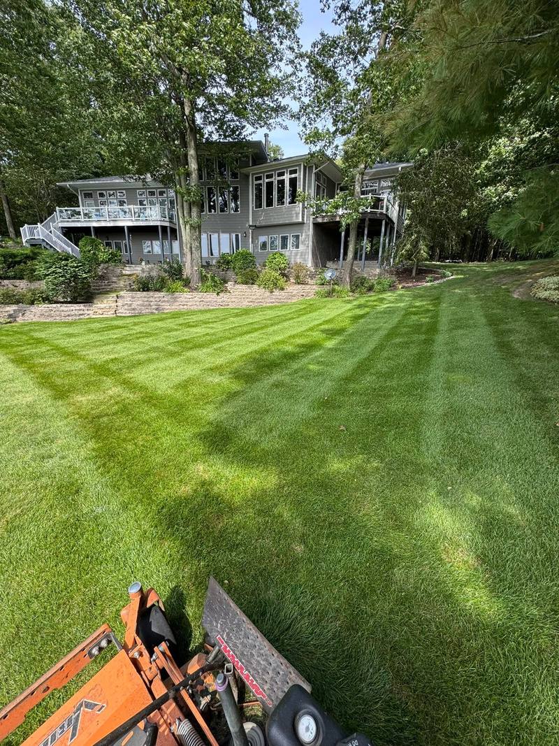 Striped lawn below a large gray home with a stone retaining wall